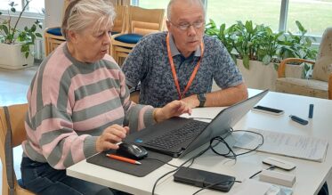 Nainen ja mies istuvat vierekkäin pöydän ääressä. Naisella on edessään kannettava tietokone.