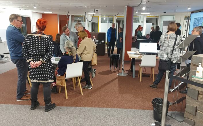 Joukko kaupunkilaisia keskustelemassa Järvenpään keskustan ja Rantapuiston kehittämisestä pop-up-tilaisuudessa. Osallistujat ja kaupungin työntekijät keskustelevat eri kehitysideoista.